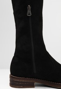 Czarna zamszowa kozaki za kolano z bocznym zamkiem i teksturowaną tkaniną. Podeszwa jest brązowa z warstwowym wzorem.