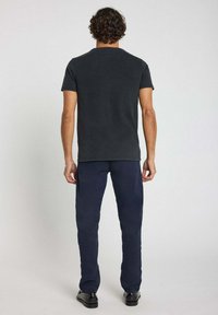 T-shirt en coton noir avec un col rond, des manches courtes et une coupe décontractée, associé à un pantalon tapered bleu marine et des chaussures noires.