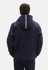 Dunkelblaue Kapuzenjacke mit einem einfarbigen Design, ausgestattet mit einem Frontreißverschluss, anpassbarer Kapuze und einem reflektierenden Streifen auf dem Rücken für bessere Sichtbarkeit.