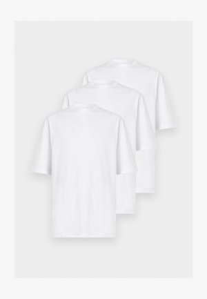 Deux personnes debout côte à côte portant des t-shirts blancs oversize, des pantalons gris larges et des chaussures noires sur un fond blanc uni.