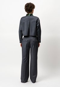 Donkergrijze cropped jas met een glinsterende groene kraag, gecombineerd met rechte broekspijpen met achterzakken en een getailleerde pasvorm.