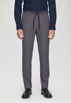 Graue Hose aus strukturiertem Stoff, mit einem elastischen Bund und einem Zugband, sowie seitlichen Taschen, kombiniert mit schwarzen Schuhen.