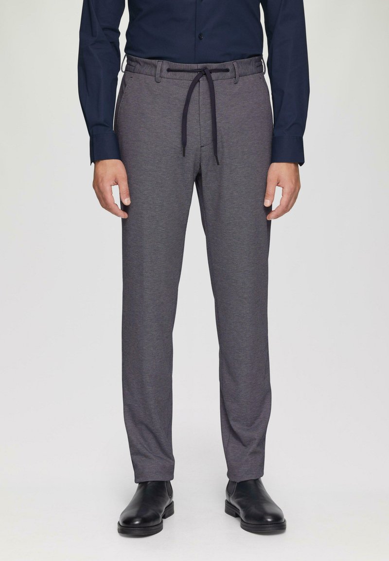 Pantalons gris en tissu texturé, dotés d'une taille élastique avec un cordon de serrage et de poches latérales, associés à des chaussures noires.