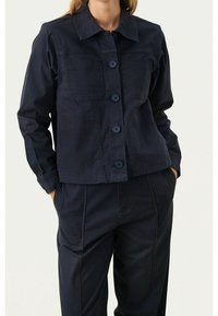 Granatowa bawełniana kurtka z kołnierzykiem, z guzikami z przodu, dwiema kieszeniami na piersiach i długimi rękawami. Gładka tekstura, krótki fason.