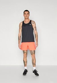 Camisola de alças atlética para homem em cinza escuro, combinada com calções laranja brilhante. Características incluem tecido macio, ajuste relaxado e logótipo visível.