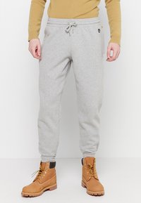 Lichtgrijze sweatpants met elastische tailleband en trekkoord, voorzien van opgerolde enkels. Gecombineerd met tan laarzen en een beige sweater.