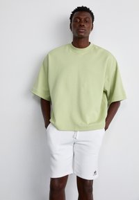 Lys grøn oversized T-shirt med korte ærmer, rund hals, lavet af blødt stof. Parret med hvide shorts med snøre og et logo.