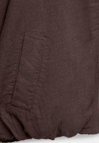 Brown, textured fabric close-up featuring a stitched pocket and gathered hem, highlighting the material's soft, casual appearance.