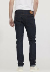 Donkerblauwe spijkerbroek van denim met een gladde textuur. Heeft twee achterzakken en een leren label op de tailleband. Slim fit ontwerp.