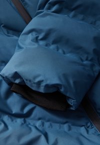 Tissu de veste matelassée bleue avec une texture lisse, dotée d'une doublure noire et de poignets élastiques. Comprend des détails de fermeture éclair et de couture.