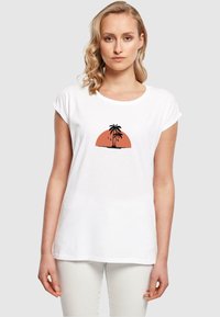 Hvid kortærmet t-shirt med et rundt grafisk motiv af en solnedgang med palmetræer i orange og sorte farver på brystet.