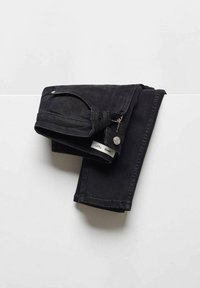 Mustat farkut, joissa on kapea istuvuus, vetoketjullinen tasku, metallinen nappi ja ompeluyksityiskohtia. Kangas on tukevaa mutta mukavaa.