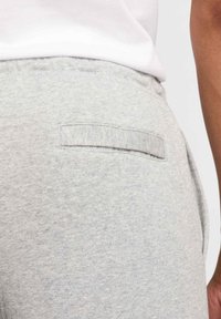 Ljusgrå träningsbyxor med en enda bakficka som har en platt, rektangulär klaff och mjuk, texturerad tyg.