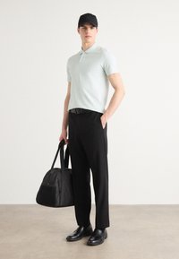 Světle modrá polokošile, černé kalhoty, černá kšiltovka a černá obuv. Nese černou sportovní tašku s zipovou kapsou.