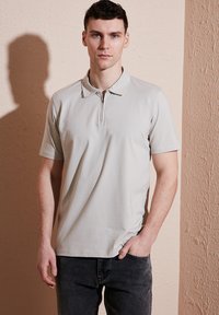 Hellgraues kurzärmliges Poloshirt mit Reißverschluss, glattem Stoff und klassischem Kragen, kombiniert mit dunklen Jeans.