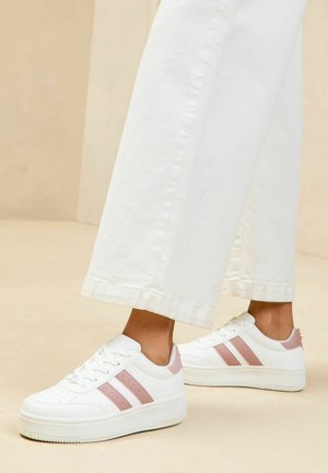 Białe sneakersy z różowymi akcentami i trzema bocznymi paskami, z zaokrąglonym czubkiem, teksturowaną powierzchnią i płaską gumową podeszwą.