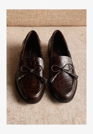 Braune Leder-Loafers mit Krokodilmuster, verziert mit einer Schleife und Quasten, sowie einer flachen Gummisohle.