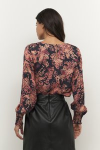 Blouse florale à manches longues, avec une base noire et un motif floral rose-orange. Détail en trou de serrure au dos, texture de tissu lisse.