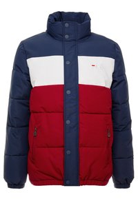 Veste rembourrée avec un design bicolore en bleu marine, blanc et rouge. Col haut, boutons-pression et poches latérales zippées pour plus de fonctionnalité.