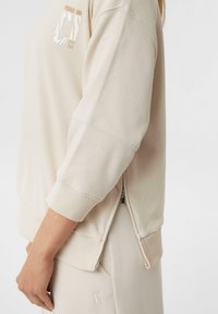 Beige sweatshirt met een relaxed fit, geribbelde mouwen en een zijritsdetail. Voorzien van een logo-opdruk op de borst en een zachte stoftextuur.