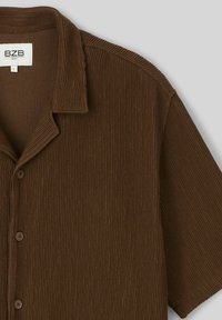 Chemise à manches courtes marron à côtes avec col, présentant une fermeture à boutons sur le devant et un tissu texturé. L'étiquette indique "BZB", taille L.