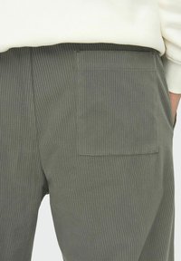 Olive-green corduroy pants feature a vertical ribbed texture and a back pocket. The material appears soft and durable.