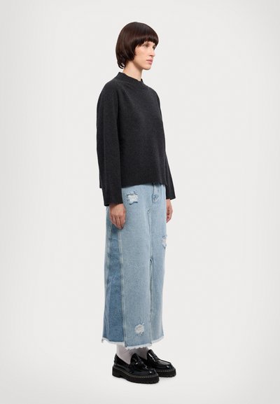 Mørkegrå strikket sweater, løs pasform, ribbet kant. Lys blå slidte denimnederdel, fransede kanter. Sorte platform sko med en blank finish.