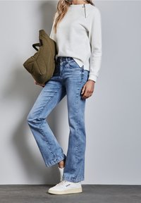 Ljusgrå texturerad tröja med dragkedjedetalj, kombinerad med ljusblå raka jeans och vita sneakers. Innehåller också en olivgrön väska.