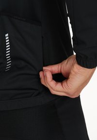 Svart idrottströja med sidoficka och reflexdetaljer. Tygstrukturen ser slät ut, åtsittande design med långa ärmar.