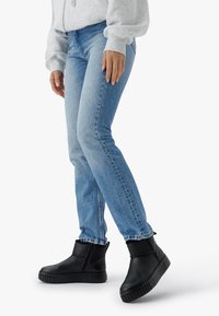 Person iført lyseblå jeans, lysegrå sweatshirt og sorte ankelhøje platformstøvler med lynlås på siden.
