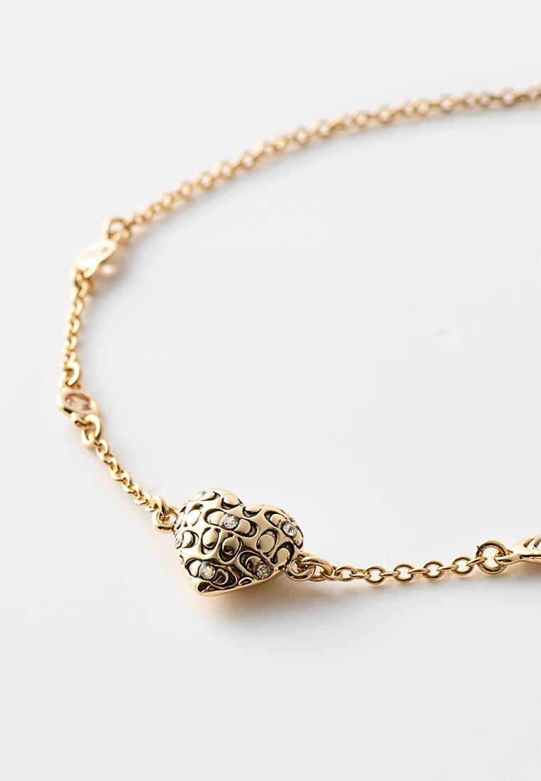 Goldene Kettenarmband mit charmantem herzförmigem Anhänger, der über strukturierte Details und eingearbeitete Strasssteine verfügt. Dezenter Glanz, leichtes Design.