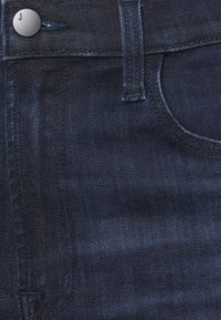 Los vaqueros de mezclilla azul oscuro presentan una textura suave, un botón plateado y un diseño clásico de cinco bolsillos con sutiles detalles de costura.