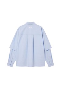 Chemise bleu clair à manches longues avec poignets boutonnés, un pli central dans le dos et un petit logo blanc près du col au dos.