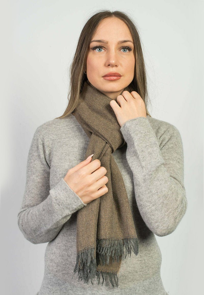 Brun ullsjal med fransiga kanter, bärs över en ljusgrå tröja. Mjuk textur och subtil design skapar en klassisk look.