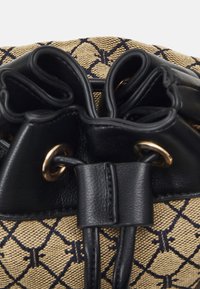 Sort læder snørrelukning på en struktureret beige stofkrop med et mønstret design, der har guldhardware detaljer.