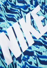 Blå og turkise mønstrede stoffer med hvit "NIKE" logo. Designet inneholder bølgende linjer og en jevn tekstur.