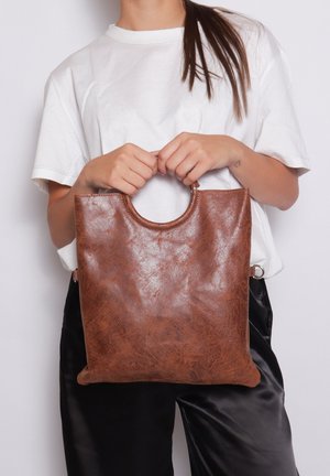 Bruine leren totesac met een gladde textuur en een ronde handgreep. Naadloos ontwerp met een ritssluiting, vastgehouden door een persoon in casual kleding.