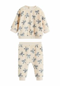 Fleece-Zweiteiler bestehend aus einem Rundhalsausschnitt-Oberteil und einer Hose mit elastischem Bund. Helles Pfirsich mit marineblauem Schleifenmuster und gerippten Bündchen. Weiche Textur.