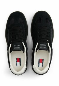 Para czarnych sneakersów Tommy Jeans z białym wyściółką i czerwono-biało-niebieskim logo marki na wkładce, widziana z góry.