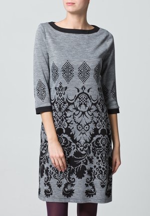 Robe grise avec un motif floral et géométrique noir, manches trois-quarts, encolure ronde et poignets noirs unis. Fabriquée en tissu doux et texturé.