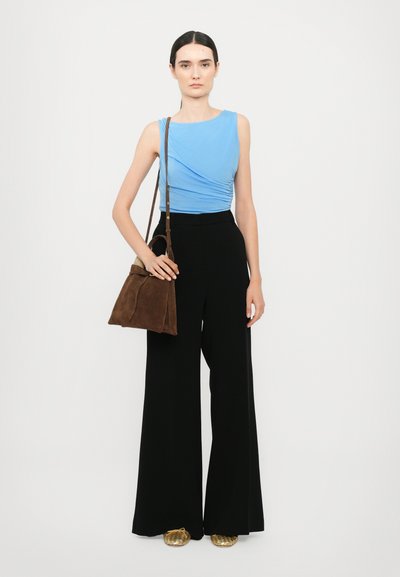 Haut ajusté bleu avec un fronce subtil, pantalon noir à jambes larges, sac à main en daim marron et chaussures dorées à enfiler. Fond neutre.