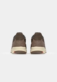 Sneaker in suede marrone con accenti neri, caratterizzati da una robusta suola bianca e un dettaglio rosso sulla suola. Mostrano "CLAE" sul tallone.
