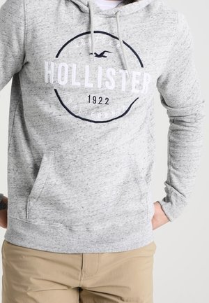 Grau melierter Hoodie mit einer Vordertasche, verstellbarer Kapuze mit Kordelzug und weißem "HOLLISTER 1922"-Logo. Material aus Baumwollmischung, mit gerippten Bündchen.