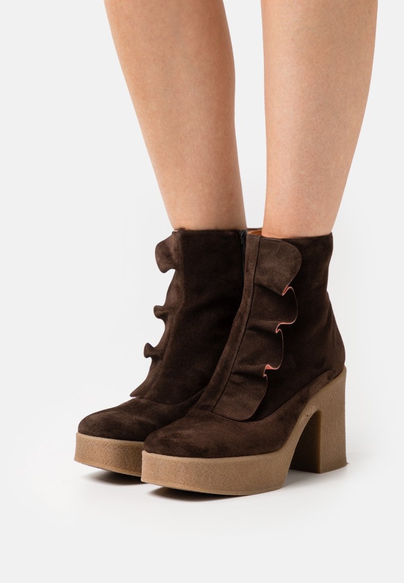 Bottines en daim marron avec détail à volants et talons compensés beige épais portées sur jambes nues.