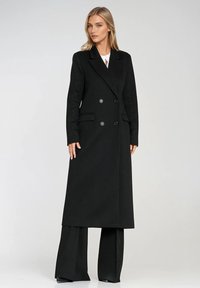Czarny dwurzędowy płaszcz o teksturowanym wykończeniu, z dwoma przednimi kieszeniami, szpiczastymi klapami i błyszczącymi guzikami. Długi, prosty krój.
