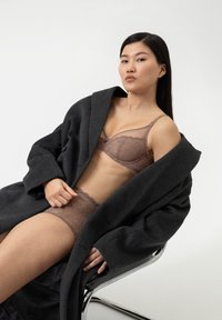 Brun spets-bikini och matchande underkläder, med blommönster och genomskinliga inslag, lagrade under en mörkgrå oversized kashmirjacka.