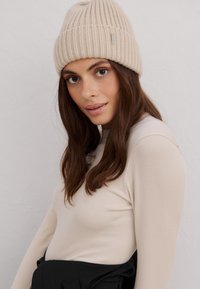 Gorro de punto acanalado beige con vuelta, llevado con una camiseta de manga larga ajustada beige claro, que presenta una textura suave.