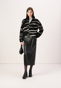 Svart og beige stripete cropped jakke i et teksturert stoff, kombinert med et svart skinn midi skjørt og kraftige svarte platå sko.