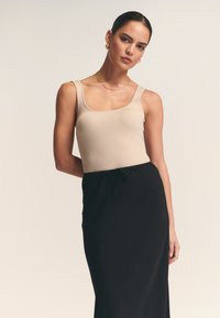 Beiger, gerippter Tanktop kombiniert mit einem schwarzen Rock mit Kordelzugbund. Der Stoff ist glatt, mit einer figurbetonten Silhouette und klaren Linien.