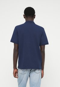 Μπλούζα πόλο με κοντά μανίκι�α σε ναυτικό χρώμα, με κλασικό γιακά. Φτιαγμένη από βαμβάκι, διαθέτει ευθεία ραφή στο κάτω μέρος και πλαϊνές σχισμές για άνεση στην κίνηση.